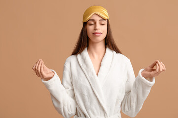 Young woman in pajamas and sleeping mask meditating on beige background