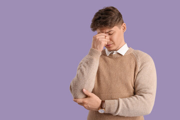 Young man suffering from headache on lilac background