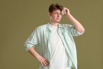 Young man with bottle of water suffering from headache on green background
