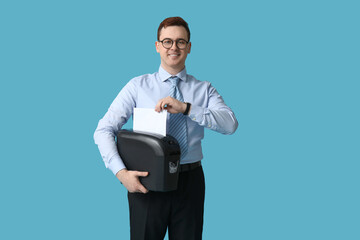 Handsome young man destroying wrong document in shredder on blue background