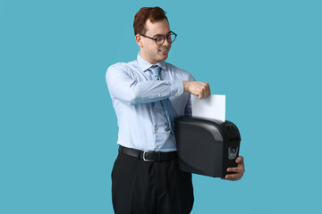 Handsome young man destroying wrong document in shredder on blue background