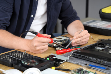 Male technician with soldering iron repairing laptop in service center, closeup