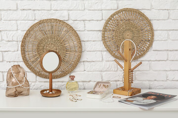 Stands with different stylish jewelry, perfume bottle and mirror on dresser near white brick wall