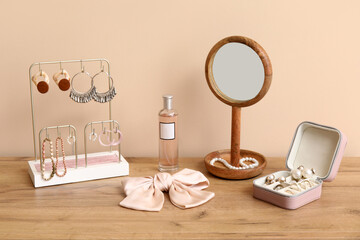 Organizers with stylish different jewelry, mirror and perfume bottle on dresser near beige wall