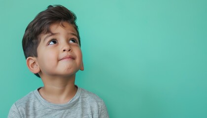 Cute boy looking up, curious and thoughtful, against a green background.