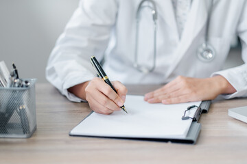 Fototapeta premium A close-up image of a doctor in a white coat writing on a clipboard at a desk in a medical office, emphasizing healthcare and professionalism.