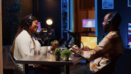 Podcast host having discussion with man, checking analog mixer to make sure audio is impeccable for...