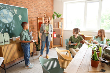 Teenage African-American boy with wind turbine model and teacher during Ecology lesson in classroom