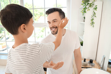 Happy father and his little son applying shaving foam on faces in bathroom