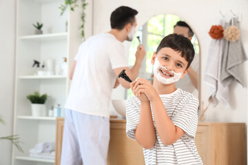 Father and his happy little son holding razors with shaving foam in bathroom