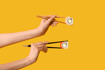 Female hands holding chopsticks with different tasty sushi rolls on yellow background
