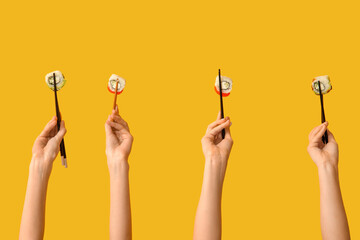 Female hands holding chopsticks with different tasty sushi rolls on yellow background