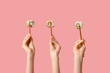 Female hands holding chopsticks with different tasty sushi rolls on pink background