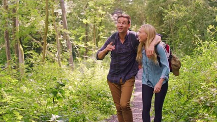 Loving couple walking along path through trees on hike with man putting arm around woman's shoulder - shot in slow motion