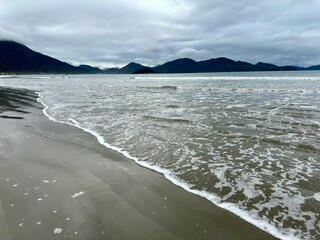 Lindo mar com ondas e o ceu escuro e fundo com montanhas.