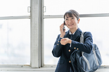 放課後に腕時計を見ながらスマホで通話する笑顔の高校生・女子高生
