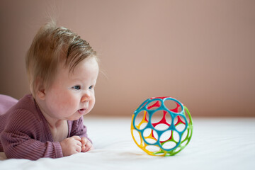 Cute Caucasian newborn baby girl during tummy time looking at the colorful ball. A 3-month-old girl with hair. Child care concept with copy space