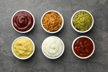 Many different sauces in bowls on grey table, top view