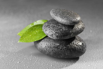 Wet spa stones and green leaves on grey background