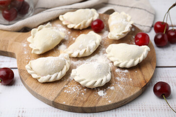 Raw dumplings (varenyky) and fresh cherries on white wooden table
