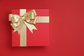 Gift box with bow on red background, top view. Space for text