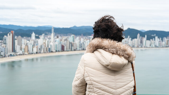 Young white brunette woman contemplating the view of the beachfront with large buildings in the background and the sea.