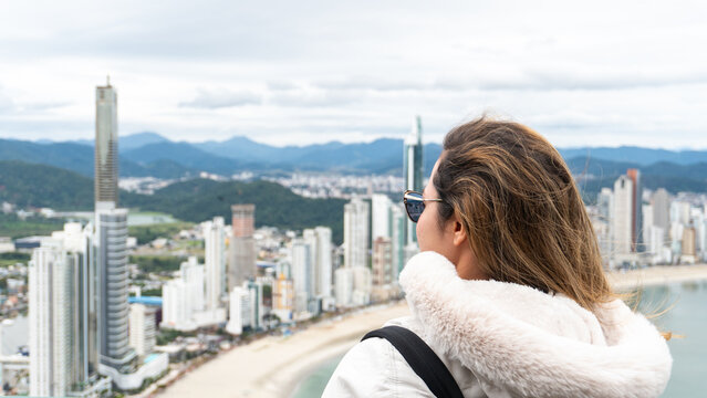 Young white brunette woman contemplating the view of the beachfront with large buildings in the background and the sea.