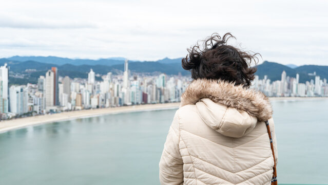 Young white brunette woman contemplating the view of the beachfront with large buildings in the background and the sea.