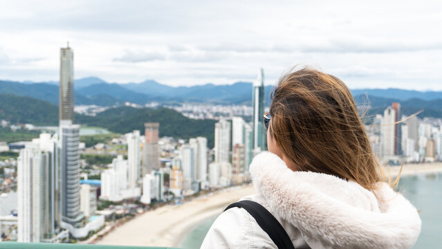 Young white brunette woman contemplating the view of the beachfront with large buildings in the background and the sea.