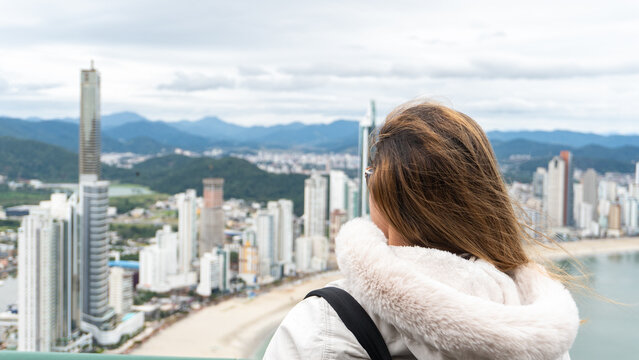 Young white brunette woman contemplating the view of the beachfront with large buildings in the background and the sea.
