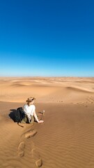 Lone traveler sitting on the sand dunes under a clear blue sky in Namibia, Africa.