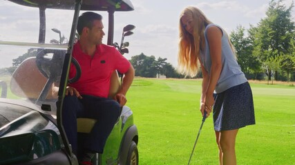 Man in golf buggy giving advice to woman as she practices with golf club - shot in slow motion