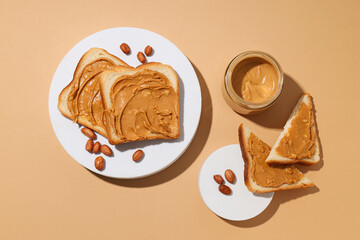 Peanut paste in a glass jar with toast, on a light background.