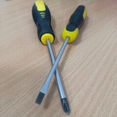 Two screwdrivers on a wooden surface, one with a flathead tip and the other with a Phillips head....