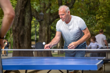 An elderly man is playing table tennis in a city park