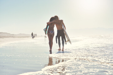 Love, hug and couple with surfboard at a beach for summer, fun and bonding on vacation in nature. Sunset, back or surfer people embrace while walking at sea for travel, romance or anniversary holiday