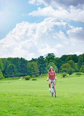 Cycling, woman and happy in countryside for eco friendly or sustainable transportation in park. Blue sky, female person and travel or freedom in nature for journey, adventure and smile for sunshine