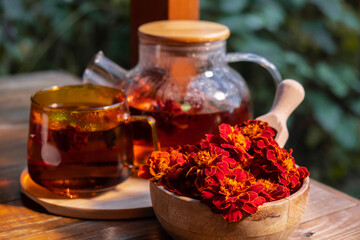 Marigold tea still life on table in green garden background. Healthy hot drink benefits. Natural organic aromatic drink in cup. Home-grown immunity-boosting herbs for tea. Autumn winter warming