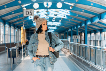 Fototapeta premium Woman Wearing Knit Hat and Denim Jacket Walks Through Bus Station