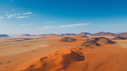 Drone shot of a vast desert landscape with sand dunes and a clear blue sky
