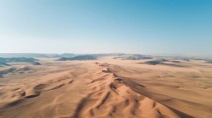 Drone shot of a vast desert landscape with sand dunes and a clear blue sky