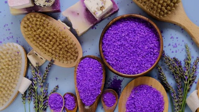 Sea lavender salt in round bowls, bath soap, natural bristle brushes, and lavender flowers are arranged on a purple background.Cosmetic spa set with lavender extract. 4k footage