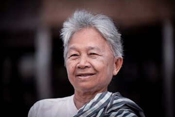 Happy elderly woman with a gentle smile. She has short, gray hair and wears a traditional outfit,...