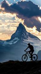 Fototapeta premium A mountain biker rides across a hilltop with the silhouette of a snow-capped mountain in the background