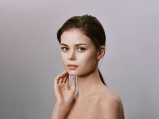 Beautiful young woman with hands on face, smiling at camera against gray background