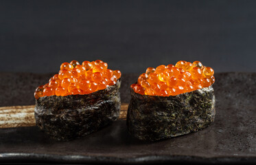 Close-up view of Gunkan Maki Sushi with salmon caviar (Ikura) On a beige Japanese plate.