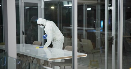 Ppe, cleaning person and table in office, disinfection and professional at night for janitor. Hygiene, protection and building for safety from virus or disease, sanitise and surface for health