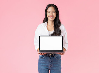 Cheerful beautiful Asian woman using laptop and looking forward on pink background.