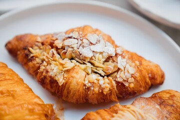 Freshly baked croissant in the brown disposable cardboard plate and a coffee in a disposable cup on a table against blurred restaurant interior background. Traditional French pastry with coffee to go
