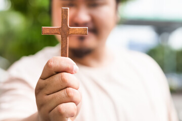 Middle-aged Asian Christian man showing wooden holy cross and praying with strong faith in...